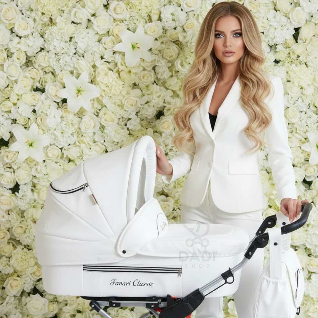 Elegancka kobieta w białym ubraniu prezentuje biały wózek wielofunkcyjny Fanari Classic na tle ściany z kwiatów.