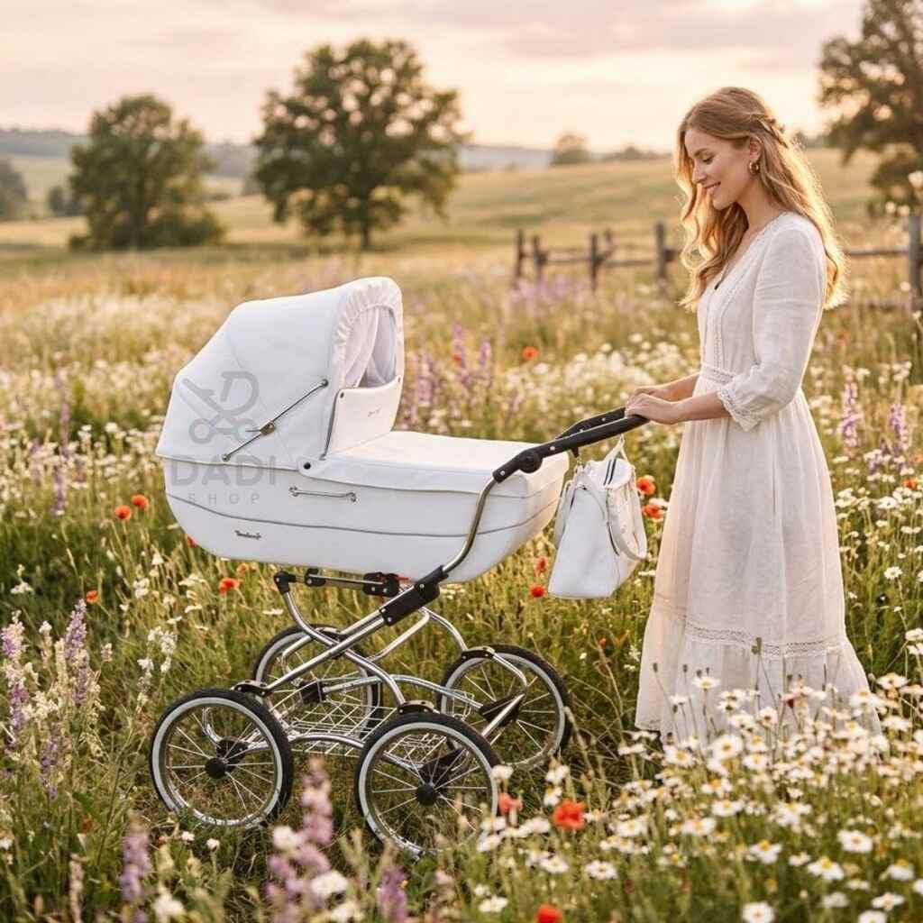 Kobieta w białej sukience spaceruje z wózkiem Baby Fashion Renee po ukwieconej łące o zachodzie słońca.