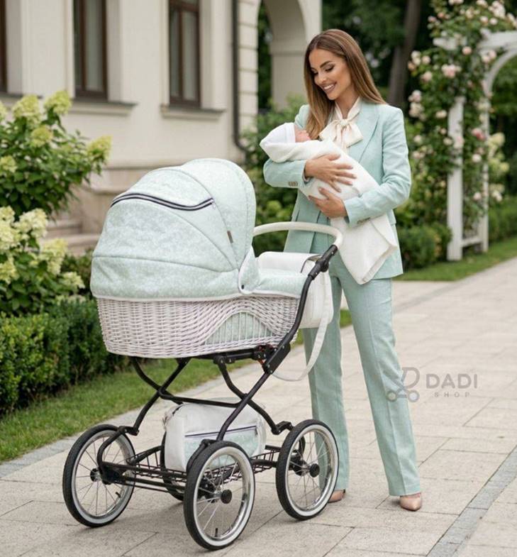 Stylowa mama w miętowym garniturze na spacerze z wózkiem retro w parku; widoczna duża gondola z plecionej wikliny.