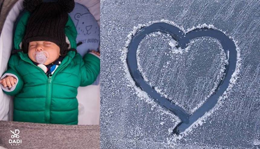 Zbliżenie na niemowlę śpiące w ciepło ubrane w wózku zimą na świeżym powietrzu, obok serce ze szronu.