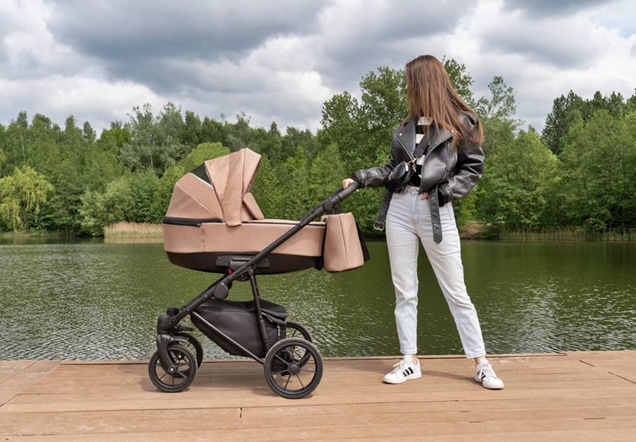 Wózek 3w1 Camarelo Alterro 07 beżowy nad jeziorem – mama pokazuje gondolę z profilu.