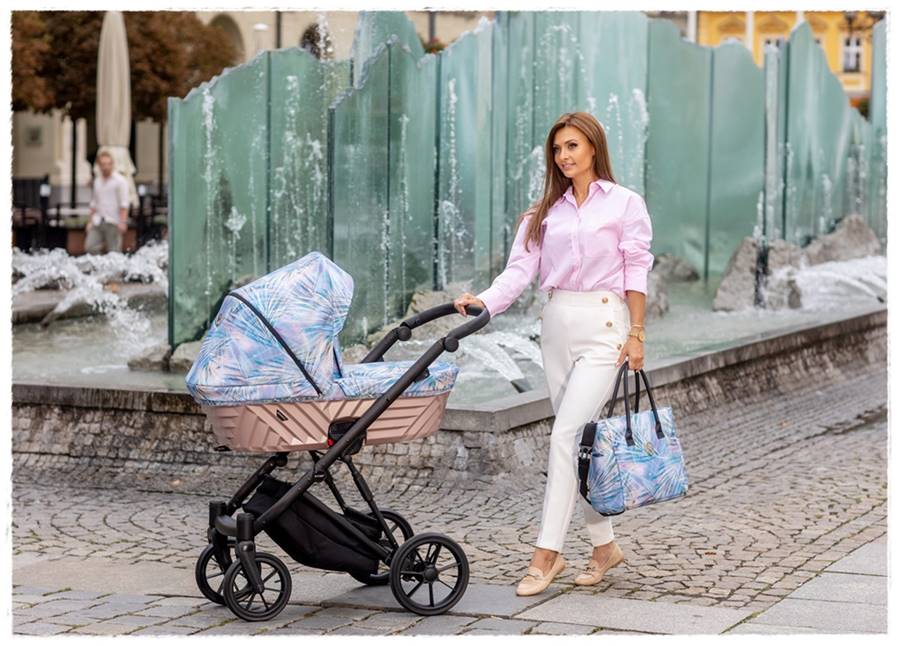 Stylowa modelka w miejskiej scenerii prezentuje wózek głęboki Kunert Ivento 2w1 Pastel Grass z gondolą i dopasowaną torbą.