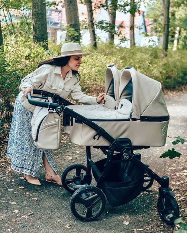 Mama pochyla się nad Junama Duo V3 Eco Beige – wózek bliźniaczy w parku, przyjazny i funkcjonalny.