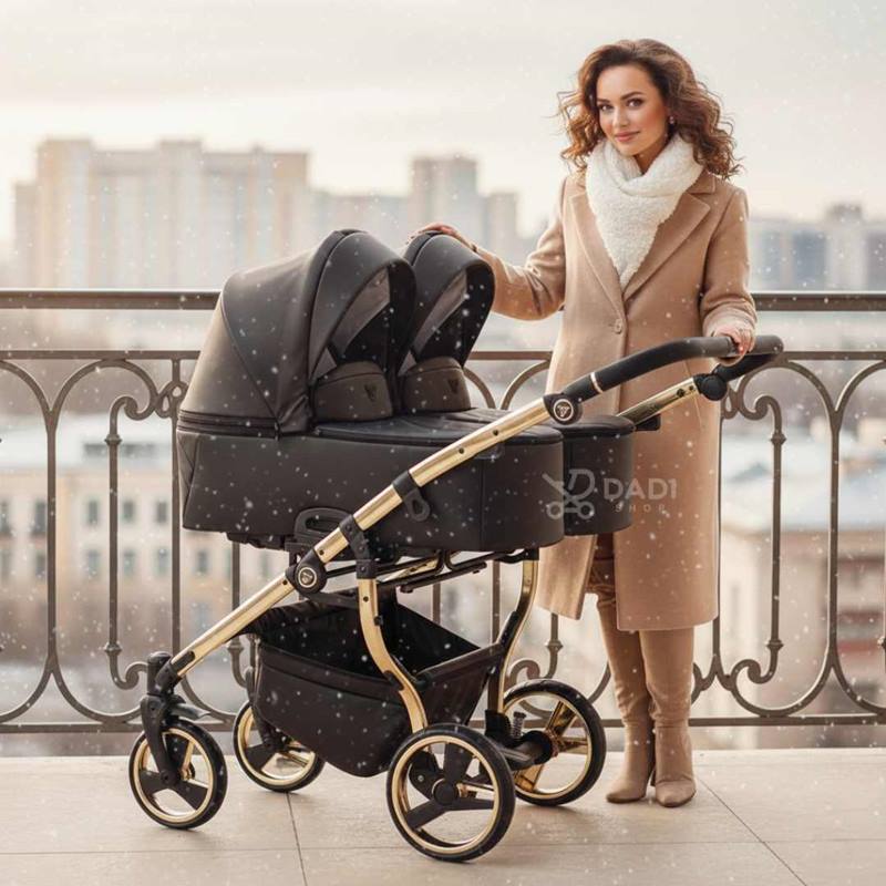 Stylowy wózek bliźniaczy 3w1 Junama Duo V3 Black & Gold zimą na balkonie, kobieta w beżowym płaszczu obok.