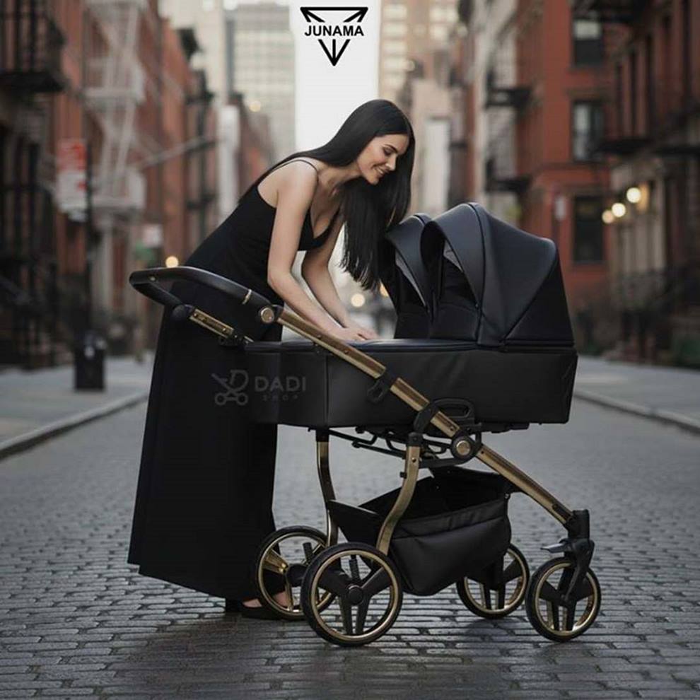 Junama Duo V3 – wózek dziecięcy bliźniaczy, czarna eko-skóra, prezentowany przez stylową kobietę w miejskiej scenerii.