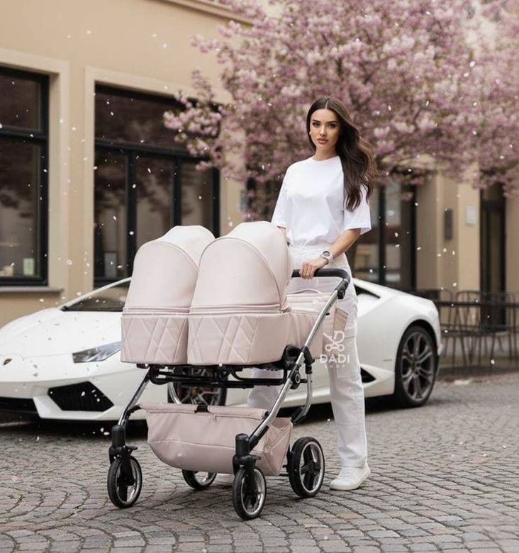 Junama Duo V3 Eco wózek dla bliźniaczek – różowy, ekoskóra, solidny stelaż, nowoczesne auto w tle.