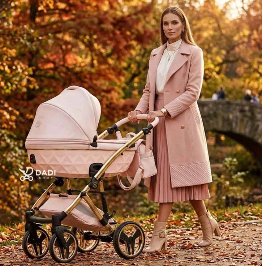 An elegant woman in a pink coat walks with a pearl-pink Junama Candy Premium baby stroller along a scenic autumn park path.