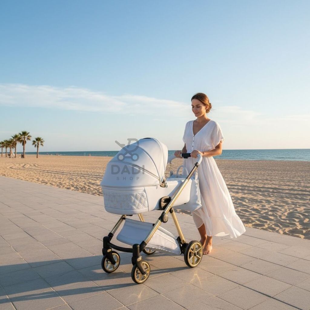 Kobieta w białej sukience prowadzi błękitny wózek Junama Ellegante Art Deco 03 Blue po nadmorskiej promenadzie. W tle piaszczysta plaża i morze.