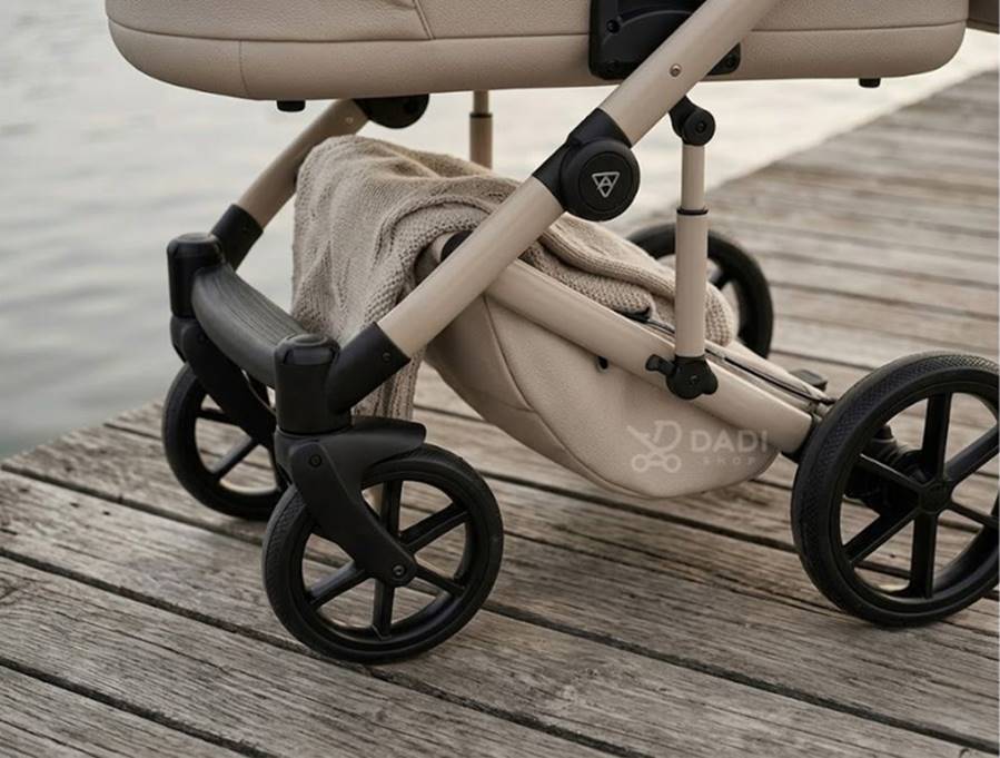 Zbliżenie na podwozie Junama Termo Elegante beżowego wózka dziecięcego stojącego na drewnianym pomoście nad wodą