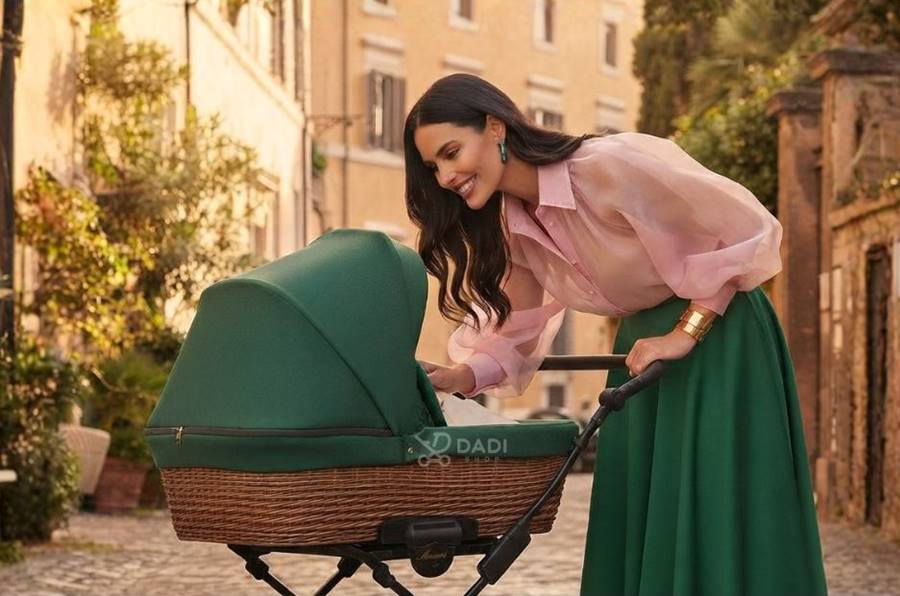 Kobieta pochyla się nad wózkiem KUNERT Romantic Classic 2w1 z wiklinową gondolą w kolorze butelkowej zieleni