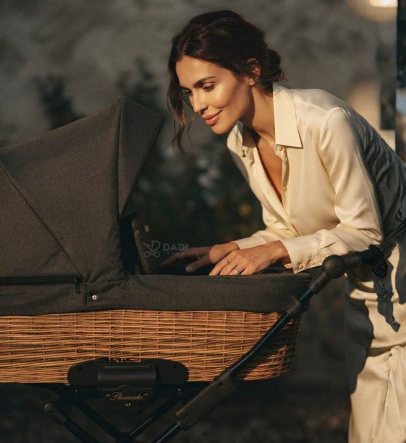 Model wózka Kunert Piemonte z naturalnym wiklinowym koszem i ciemnoszarą tapicerką, prezentowany przez elegancką mamę patrzącą do środka.