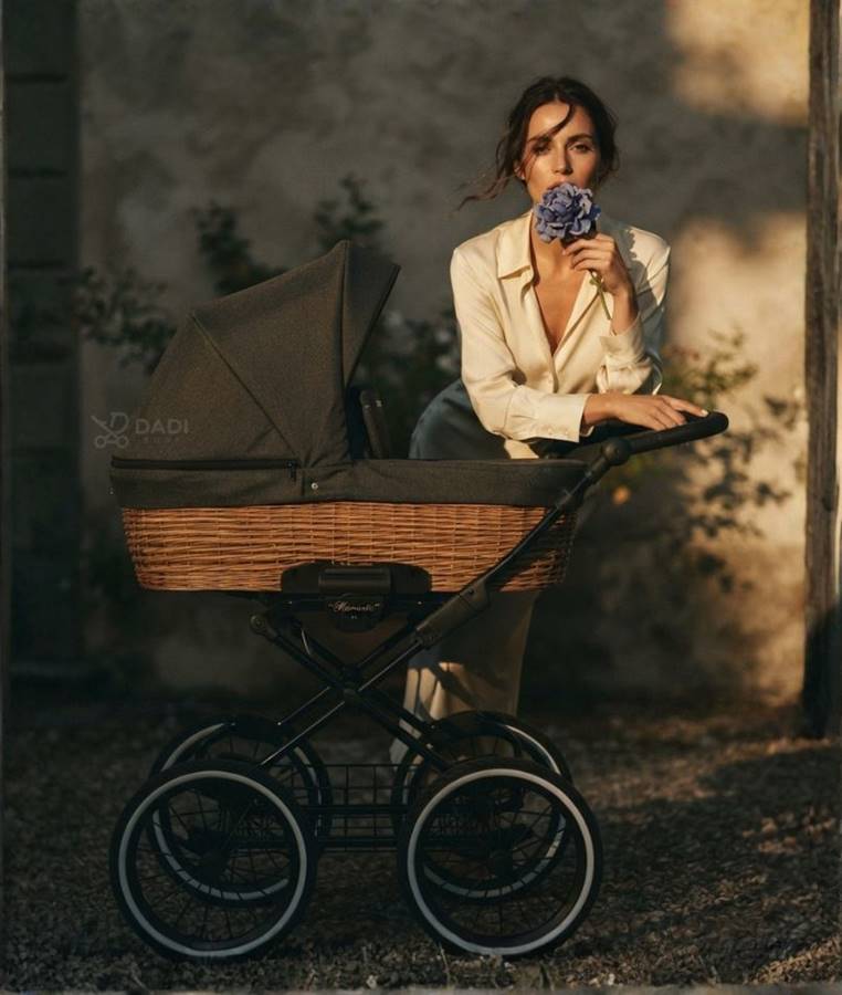 Elegancka mama z kwiatem stoi przy klasycznym wózku dziecięcym Kunert Romantic Classic na tle starego muru.