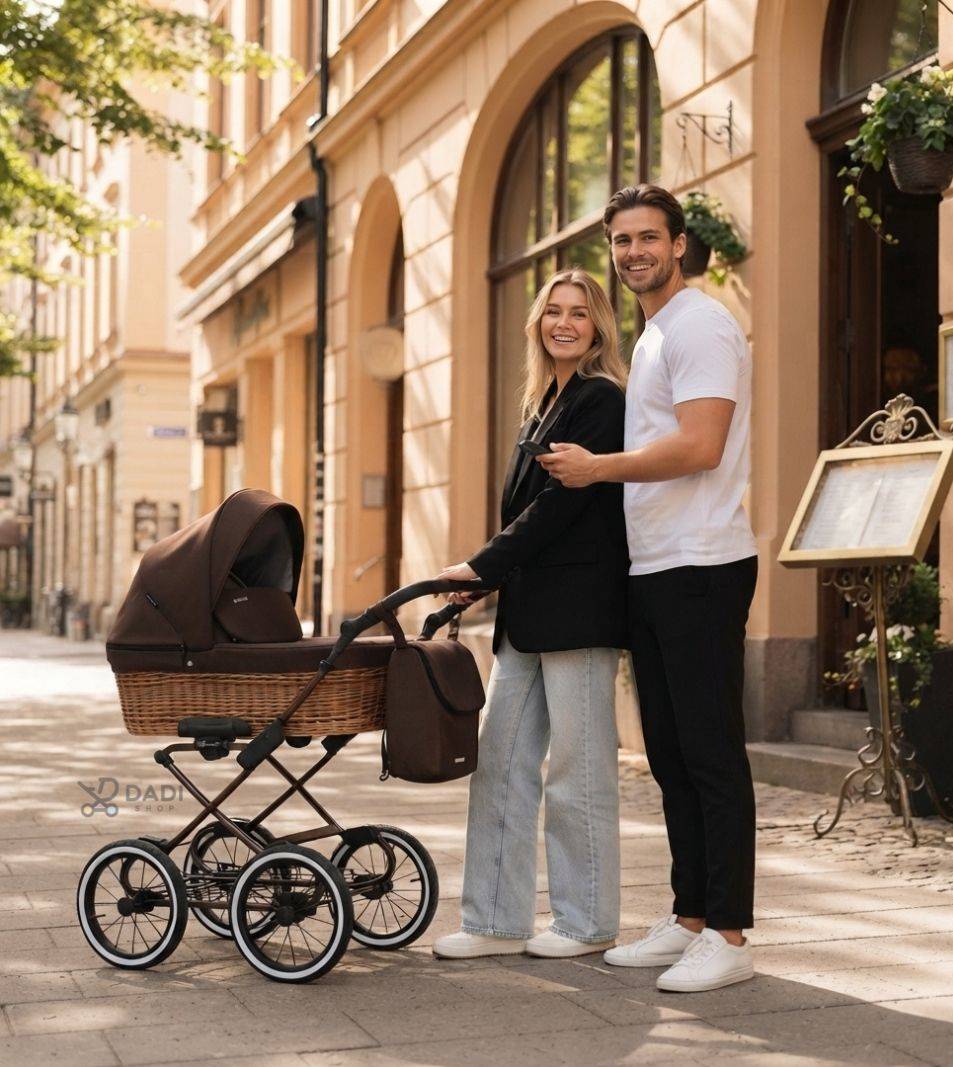 Uśmiechnięta para stoi na brukowanej ulicy starego miasta z wózkiem głębokim Kunert Romantic Classic w kolorze brązowym, z wiklinową gondolą i dużymi kołami.