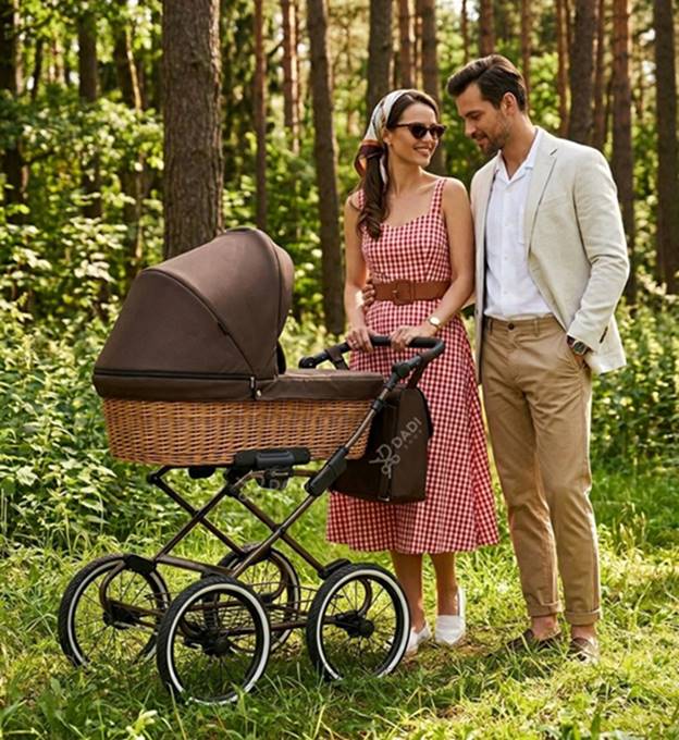 Wózek głęboki retro Kunert Romantic Classic – brązowa wiklinowa gondola na klasycznym stelażu z dużymi kołami podczas spaceru rodziców w lesie