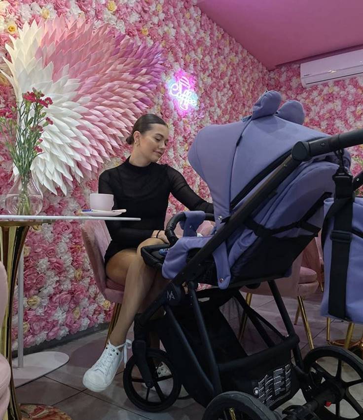 Spacerówka Natoni Joy New w kolorze Ver Peri, widok z tyłu, jasnofioletowe tło, mama z wózkiem – prezentacja lifestyle w sklepie Dadi Shop.