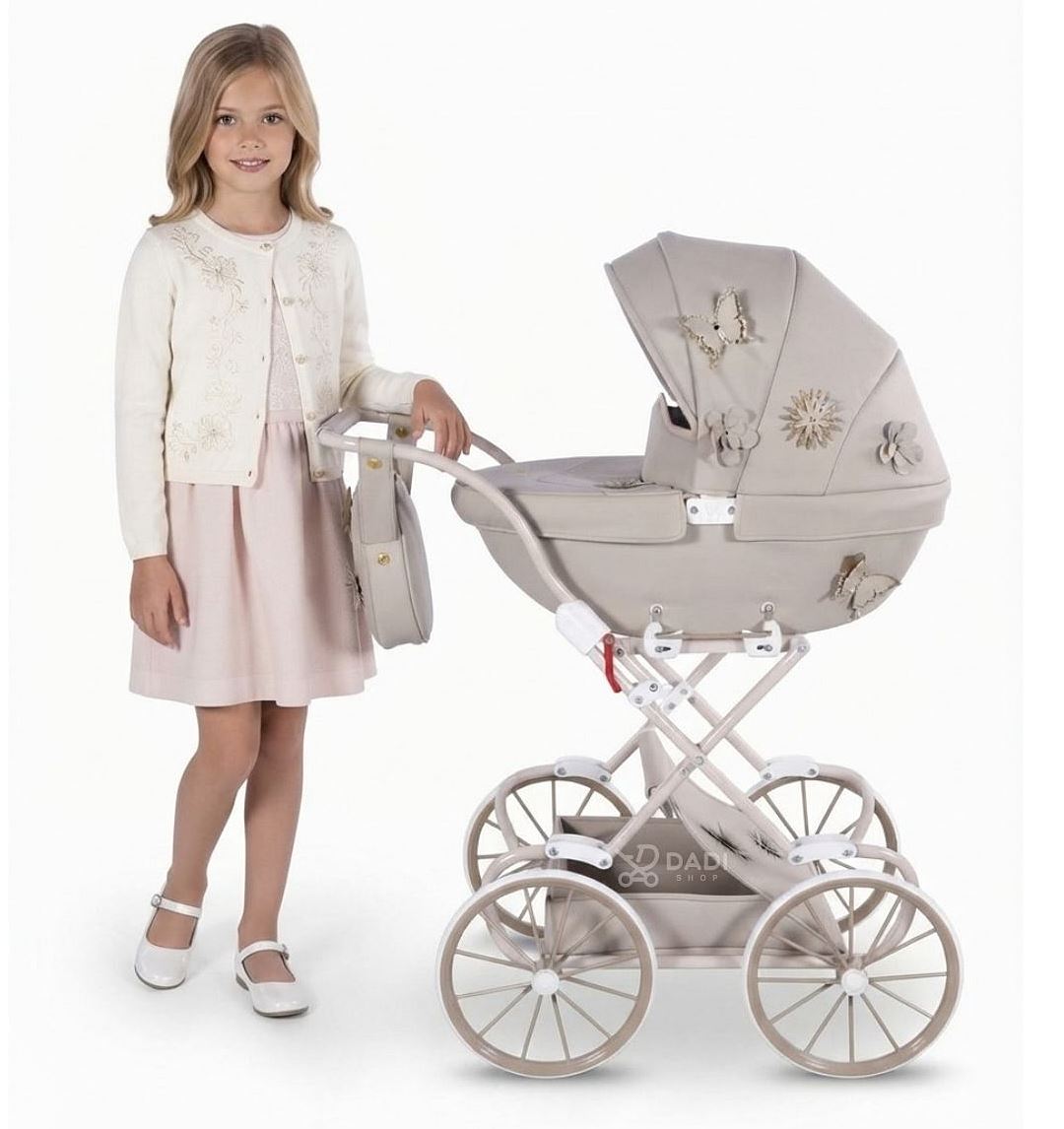Wózek dla lalek Junama Fleur Mini 02 Beige w stylu retro, ozdobiony aplikacjami motywów florystycznych. Prezentowany z uśmiechniętą dziewczynką