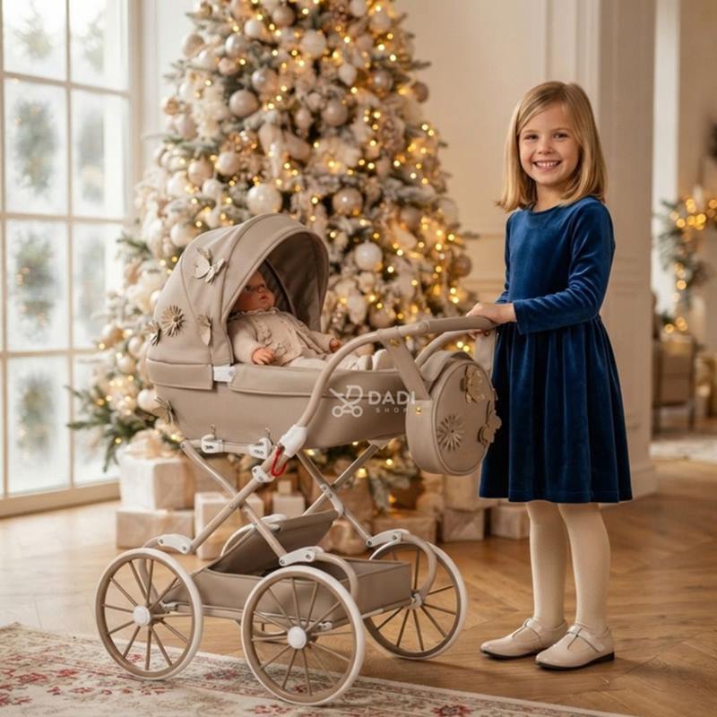 Wózek retro dla lalek Junama Mini Fleur Beige z lalką w gondoli obok oświetlonej choinki.