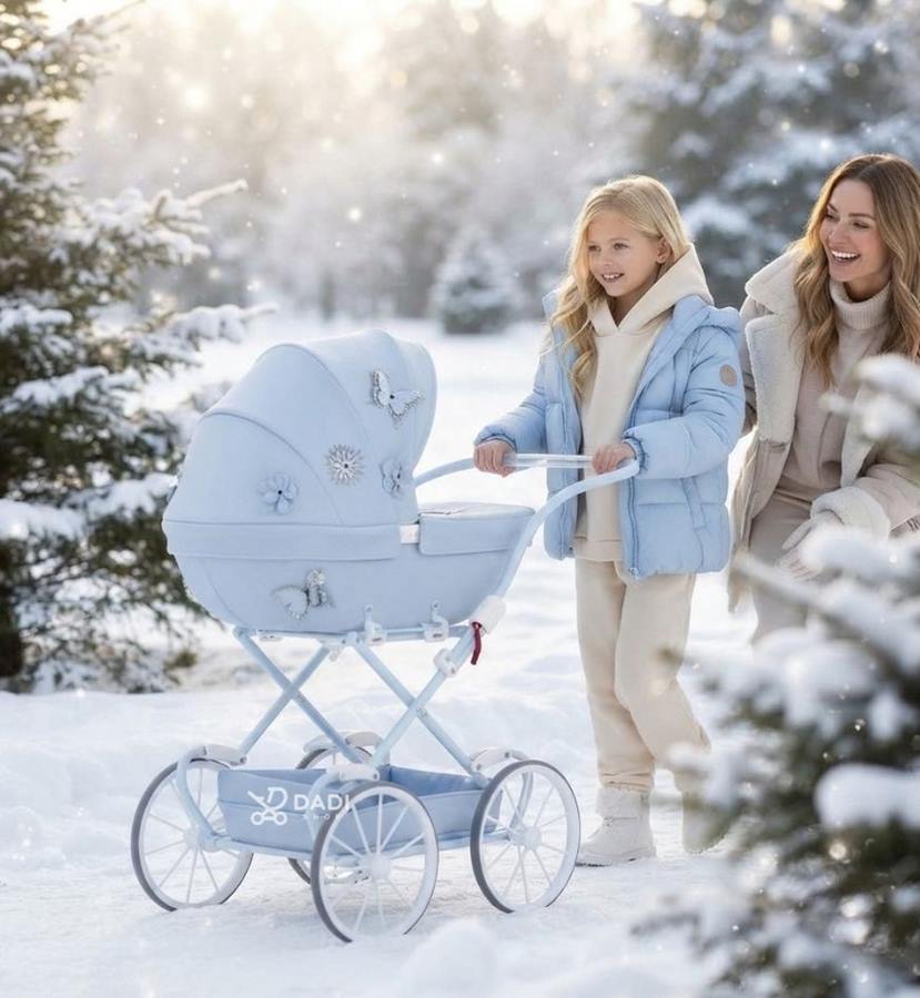 Dziewczynka w kurtce i mama spacerują z błękitnym wózkiem dla lalek Junama Mini Fleur wśród ośnieżonych drzew.