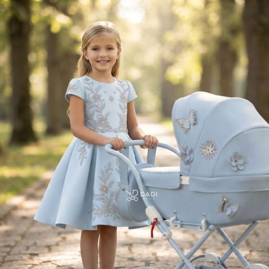 Starsza dziewczynka pozuje z wózkiem dla lalek Junama Mini Fleur podczas słonecznego spaceru w parku.
