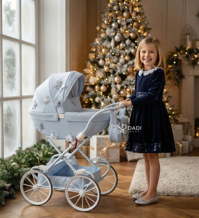 Uśmiechnięta dziewczynka w eleganckiej sukience pozuje z błękitnym wózkiem dla lalek Junama Mini Fleur przy przystrojonej choince