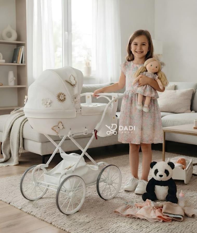 7-letnia dziewczynka w jasnym salonie trzyma lalkę obok wysokiego wózka dla lalek Junama Mini Fleur White na retro stelażu, z pluszową pandą i ubrankami na dywanie.