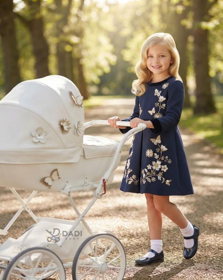 Dziewczynka w eleganckiej sukience z białym wózkiem dla lalek Junama Mini Fleur w parku.