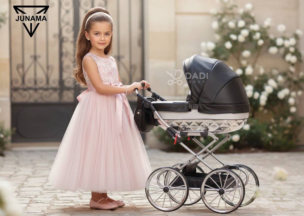 A little girl walking with her Junama Hand Craft Glitter white-gold dolls pram during a stylish spring outdoor session. Dadi-shop