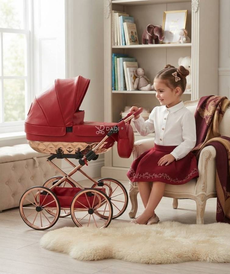 Dziewczynka siedzi w jasnym pokoju dziecięcym obok eleganckiego, czerwonego wózka lalkowego Junama Rudolf z detalami w kolorze różowego złota.