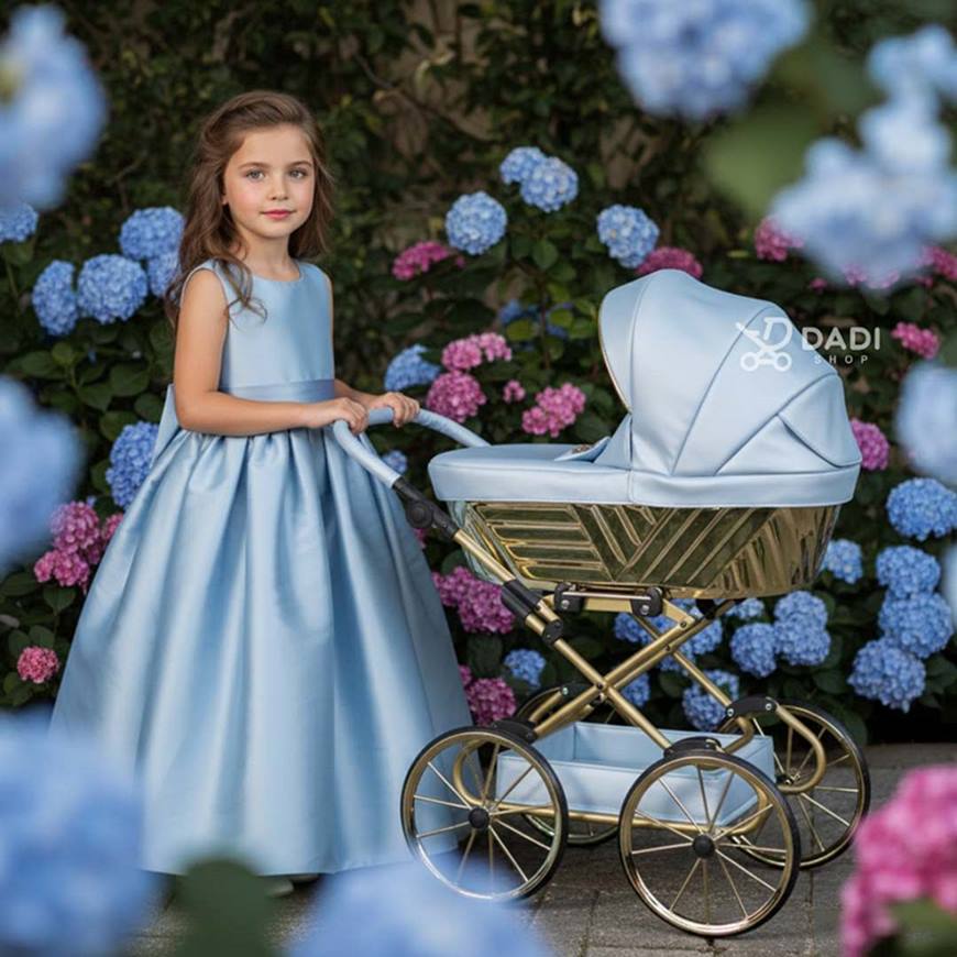 A little girl in a garden surrounded by flowers presents the blue Sojan Royal doll stroller – elegant and playful toy.